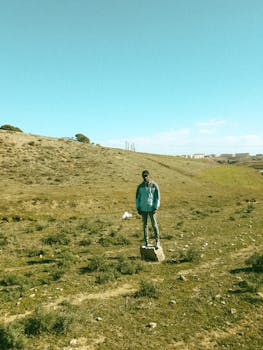 Man in blue jacket standing on stone amidst green landscape in Sétif, Algeria.